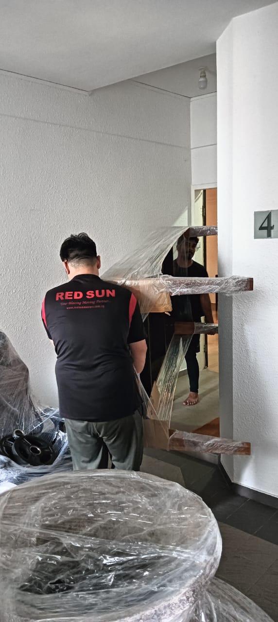 Professional movers securing furniture with protective wrapping before transport during a home move in Singapore.