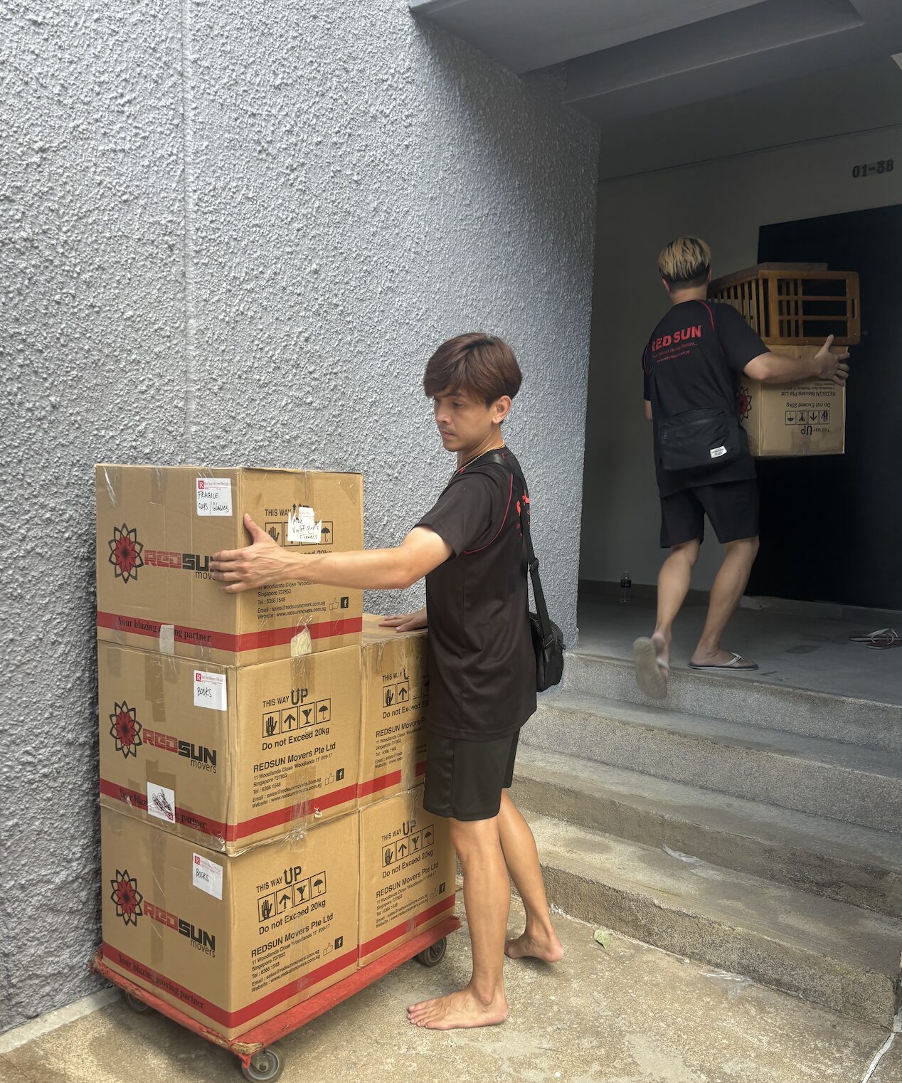 Professional movers handling packed household boxes at a condominium entrance in Singapore.